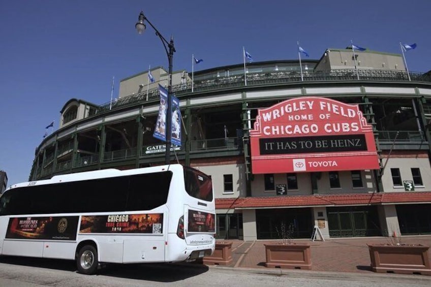 A white bus parked in front of Wrigley Field, the home of the Chicago Cubs, with a large red sign and flags. 1