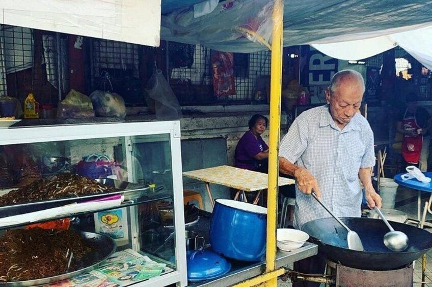 A street food vendor cooking at a stall with a large wok and various cooking utensils. 1