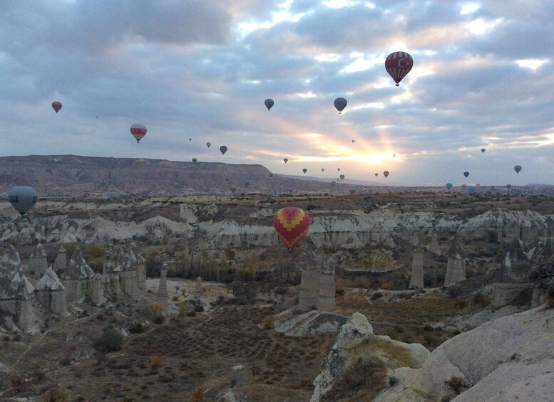 A landscape with numerous hot air balloons, rocky terrain, and a cloudy sky. 5
