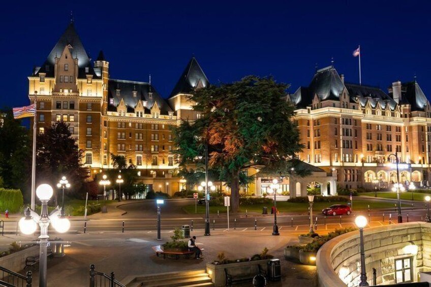A grand hotel with a large tree in front, illuminated street lamps, and a flag on top. 4