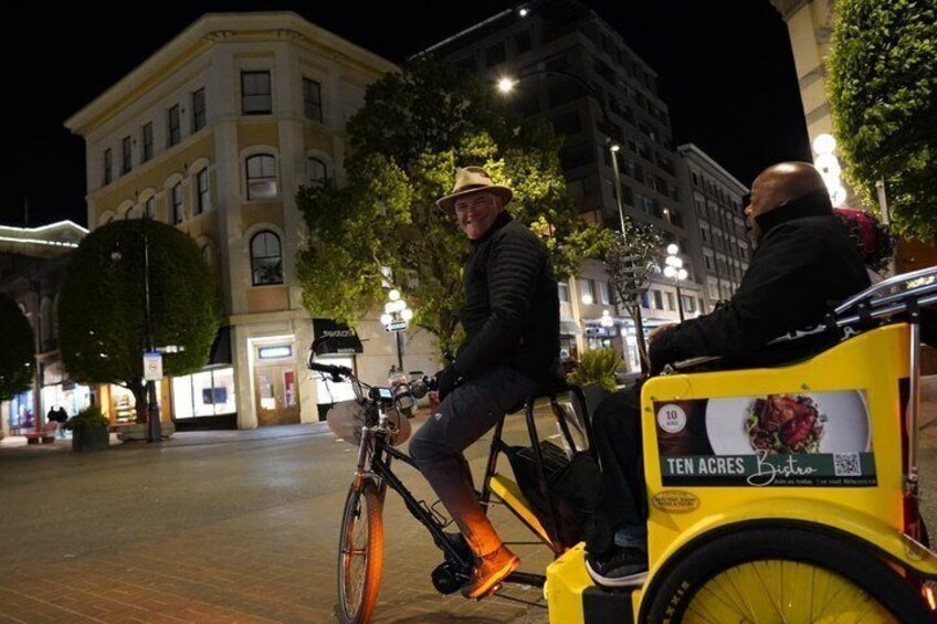A person riding a bicycle with a yellow cart, a building with illuminated windows, and a street lamp. 5