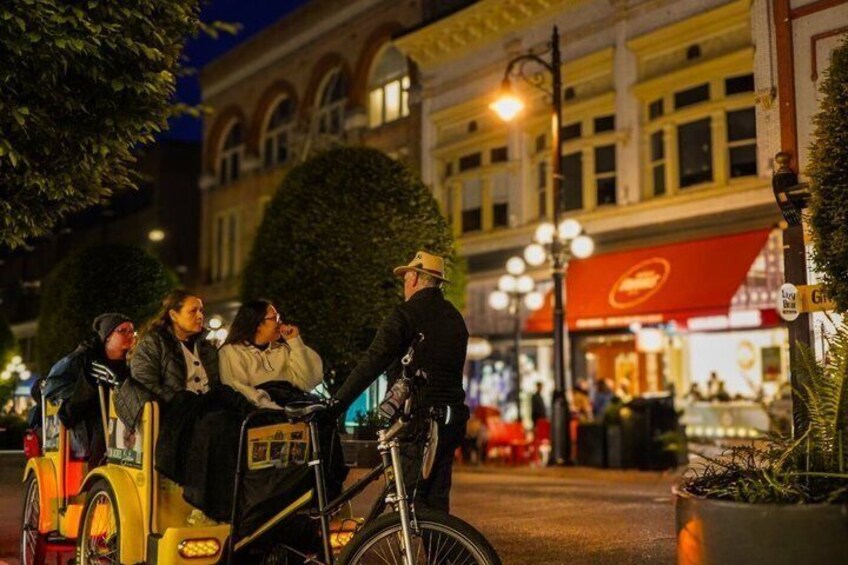 A nighttime street scene with a person on a bicycle, a group of people sitting on a yellow vehicle, and a building with a red awning in the background. 3