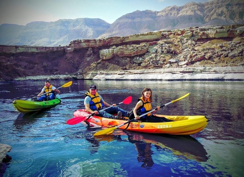 Three people kayaking on a calm river with mountains in the background. 1