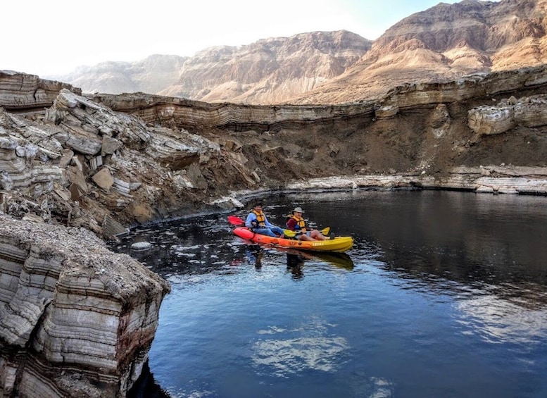 Two people kayaking on a calm river surrounded by rocky cliffs. 3