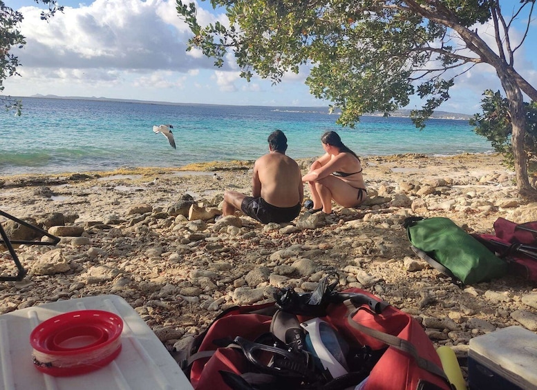 A couple sitting on a rocky beach with a red kayak and a green bag nearby. 2