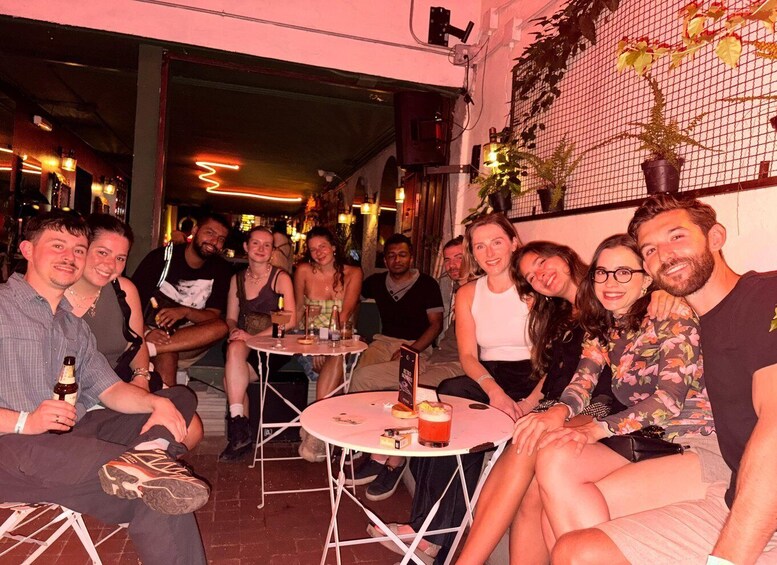 A group of people seated around tables in an indoor setting with a brick wall and hanging plants. 2