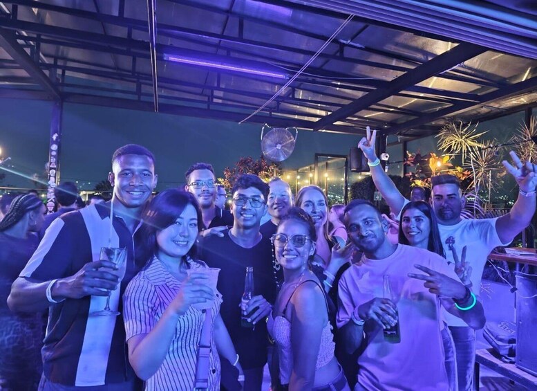 A group of people at an outdoor event with a metal roof structure and decorative lights. 5