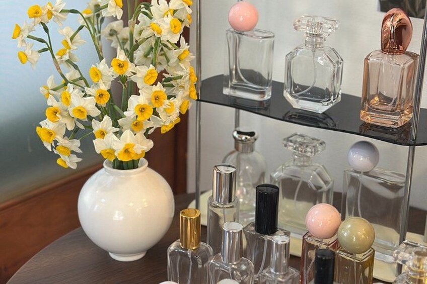 A white vase with yellow and white flowers, a glass perfume bottle, and a rose gold perfume bottle on a black shelf. 4
