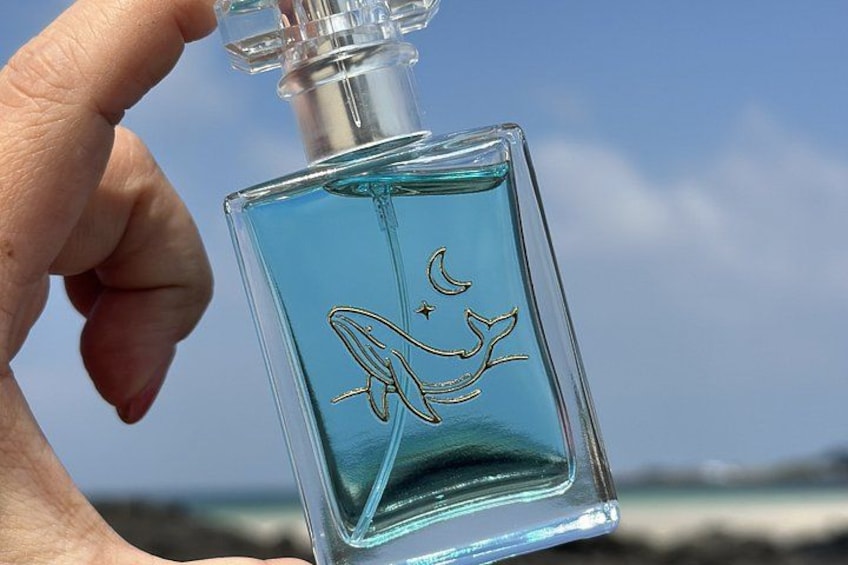 A hand holding a clear glass bottle with a blue liquid and a gold design. 1