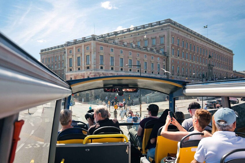 A bus with passengers, a large building in the background, and a clear sky. 1