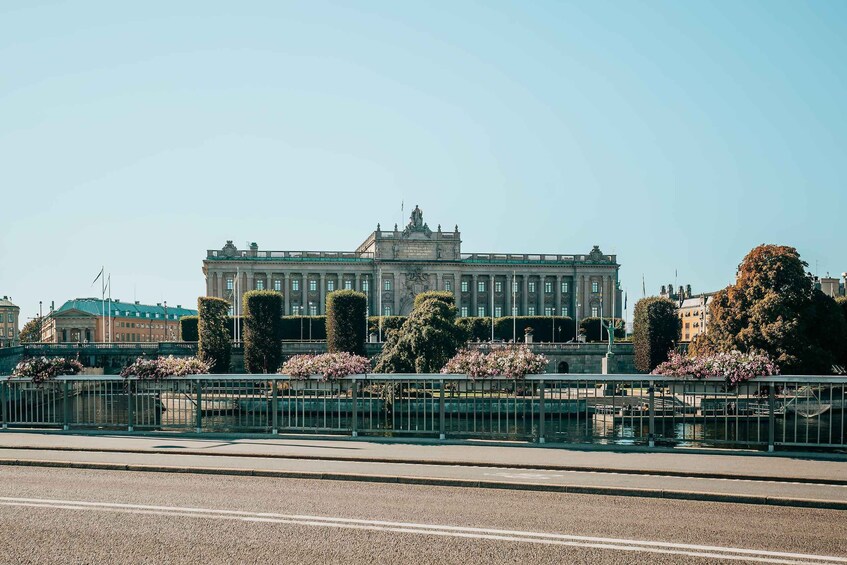 A grand building with a statue on top, surrounded by neatly trimmed hedges and flowering plants. 2