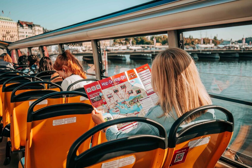 A person reading a map on a bus with a view of a river and buildings in the background. 4