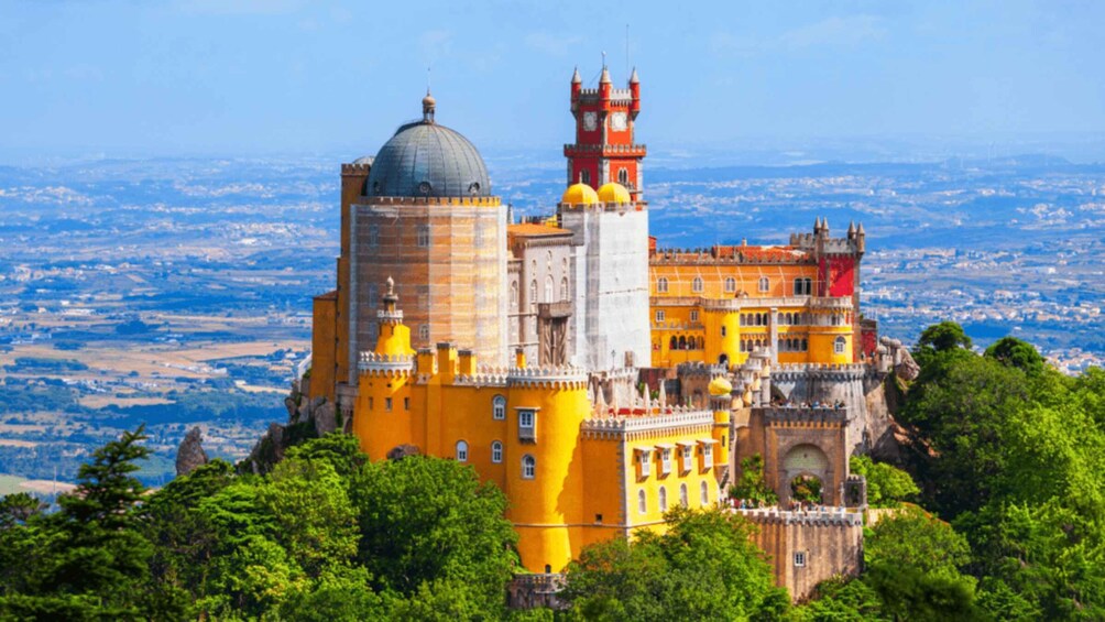 Pena Palace with its distinctive yellow facade and red tower, surrounded by lush greenery and overlooking a vast landscape. 4