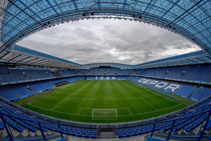 A large, empty stadium with blue seats and a green field. 2
