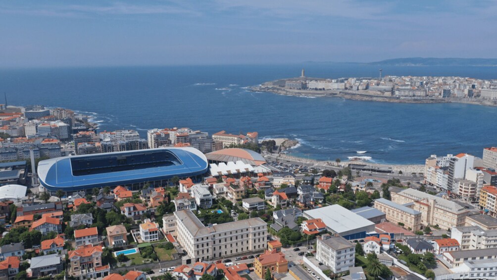 An aerial view of a coastal city with a large blue stadium, historic buildings, and the sea. 5