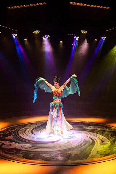 A performer on stage with a colorful, patterned floor and spotlights. 3