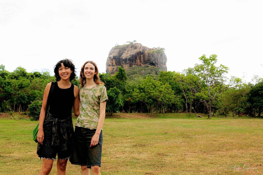 Two people standing in a grassy field with a large rock formation in the background. 3