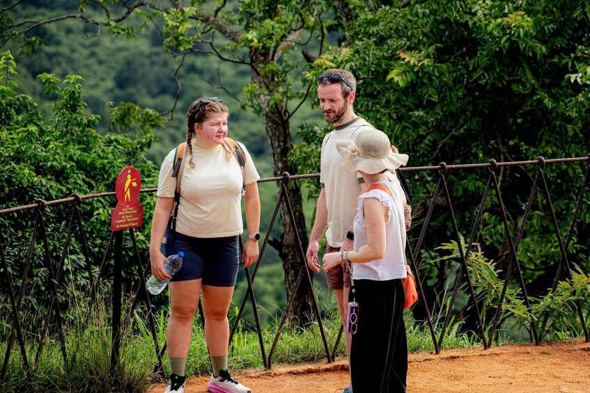 Three people standing by a rope barrier in a forested area with a sign indicating a walking trail. 5