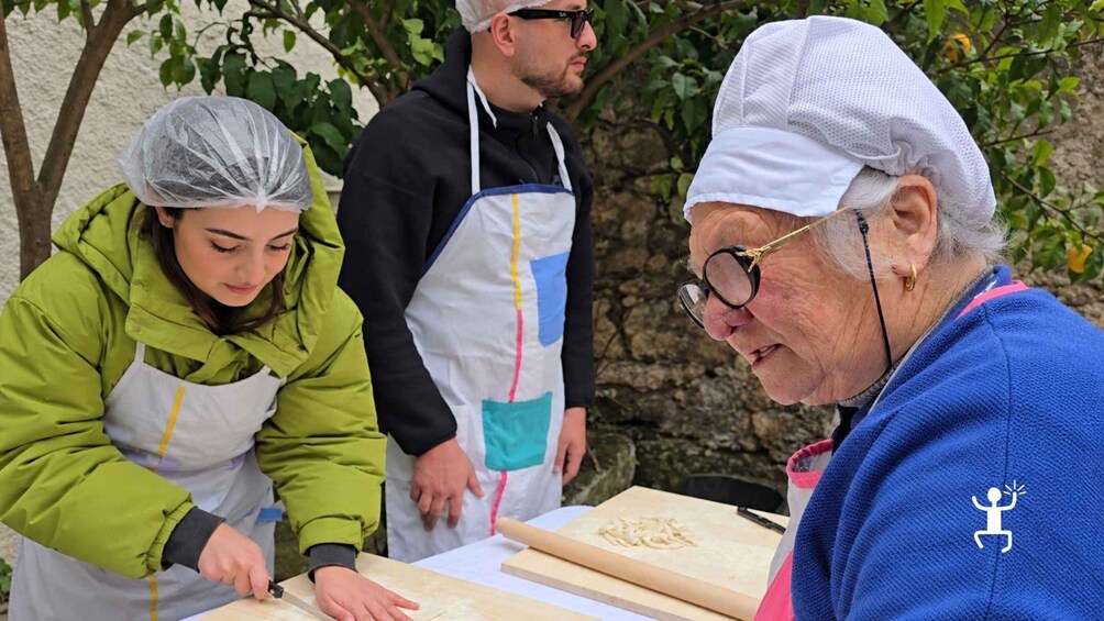 Three people preparing food outdoors, with one person cutting vegetables on a cutting board. 4