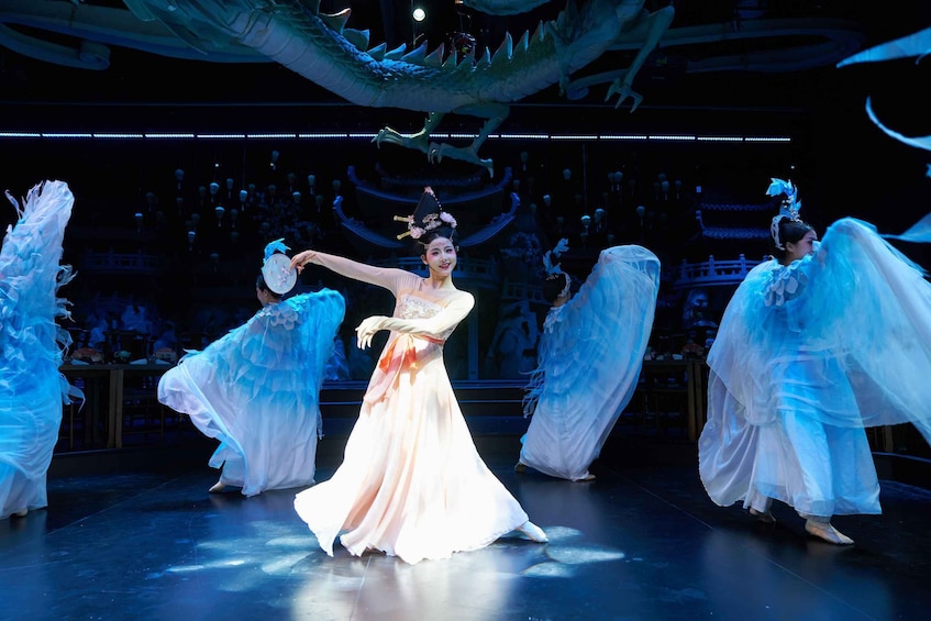 A stage performance with dancers in white and blue costumes, a dragon prop, and traditional Chinese architecture in the background. 2