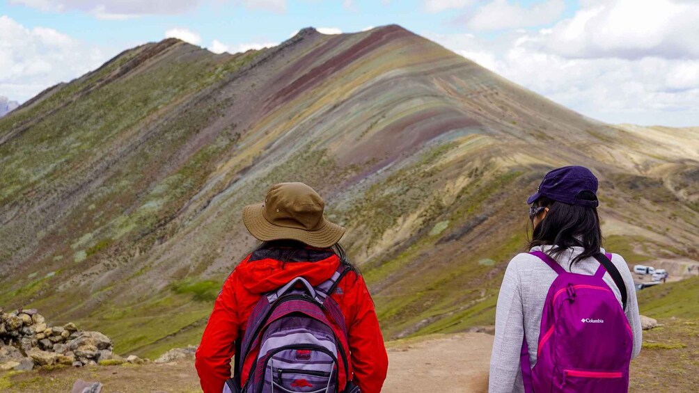 Two hikers with backpacks facing a mountain with layered rock formations. 4