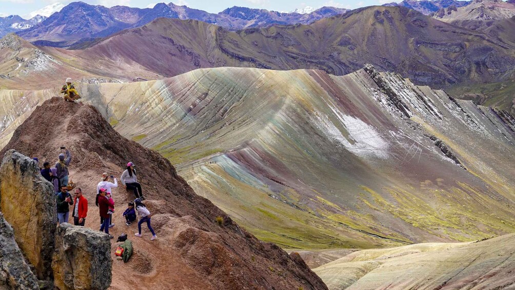 A group of people hiking on a colorful mountain ridge with a backdrop of snow-capped peaks. 2