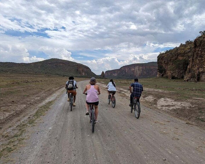 A group of cyclists on a dirt road with a mountainous landscape in the background. 1