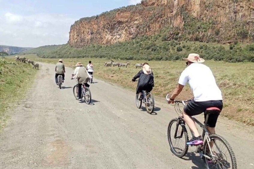 Cyclists on a dirt road with a cliff in the background. 1
