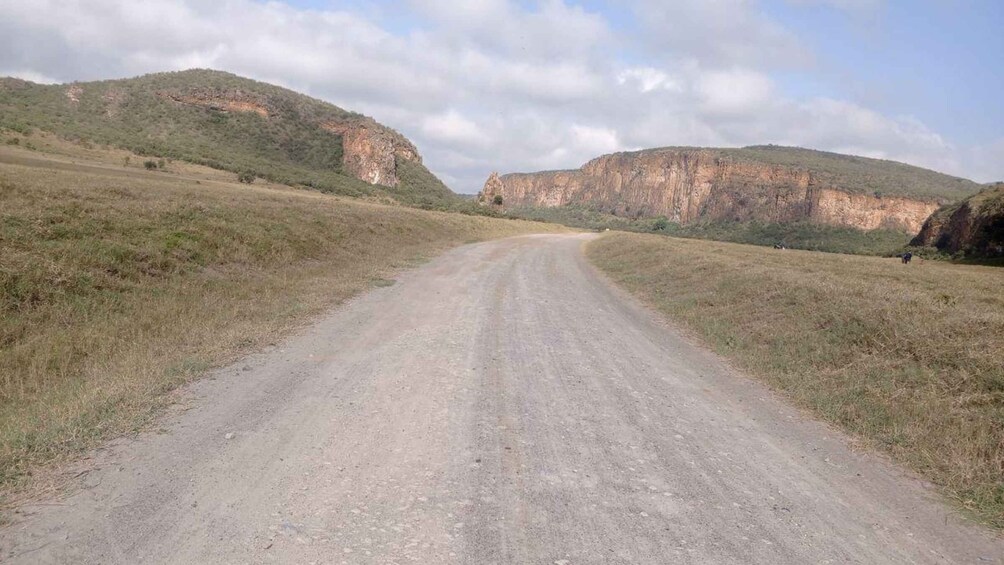 A dirt road winding through a hilly landscape with sparse vegetation and cliffs in the distance. 5