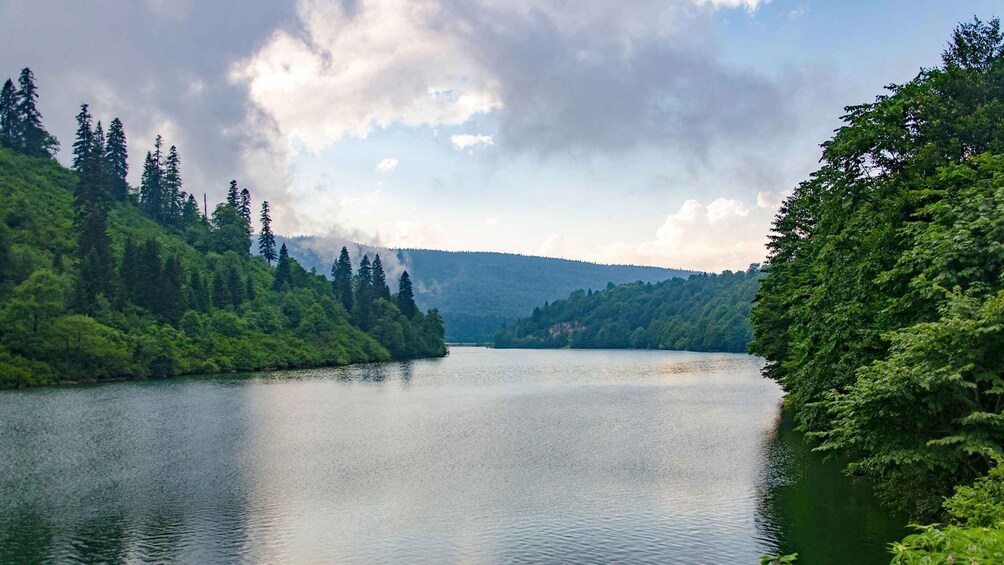 A calm lake surrounded by dense forest and mountains under a partly cloudy sky. 2