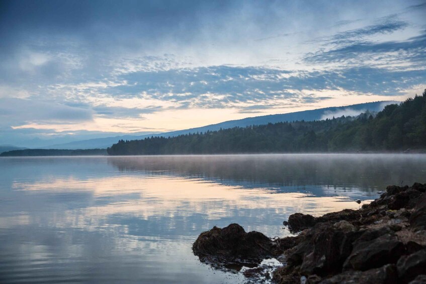 A calm lake with mist over the water, surrounded by a forested hillside. 5