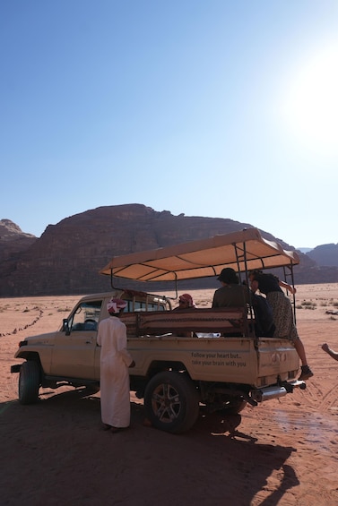 A desert landscape with a beige off-road vehicle parked on the sand, surrounded by rocky hills. 4