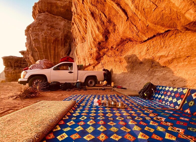 A white pickup truck parked in a desert with a colorful carpet and a large rock formation in the background. 1