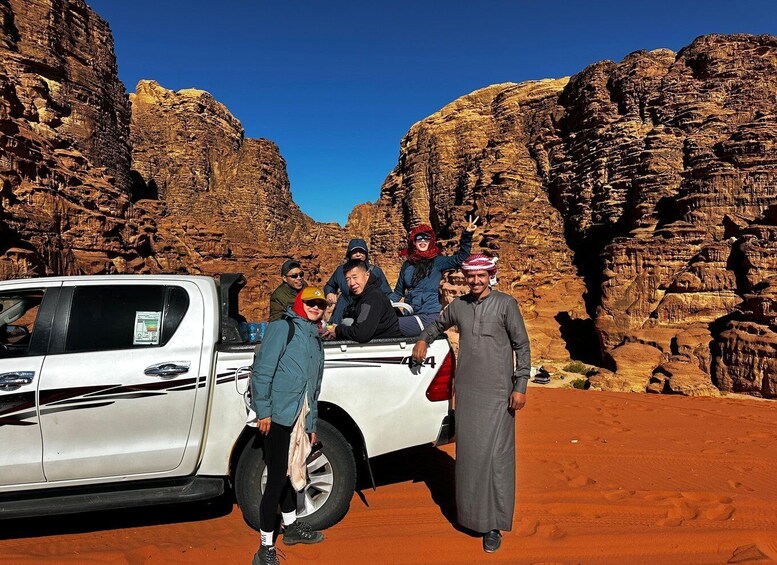 A group of people standing in front of a white pickup truck with a desert landscape in the background. 2