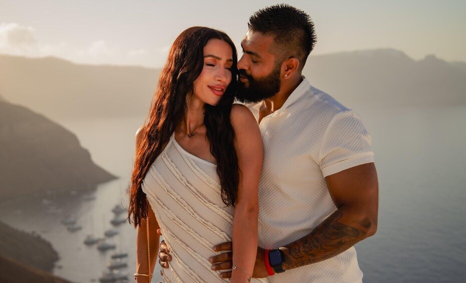 A couple embracing by a coastal area with boats in the water and hills in the background. 3