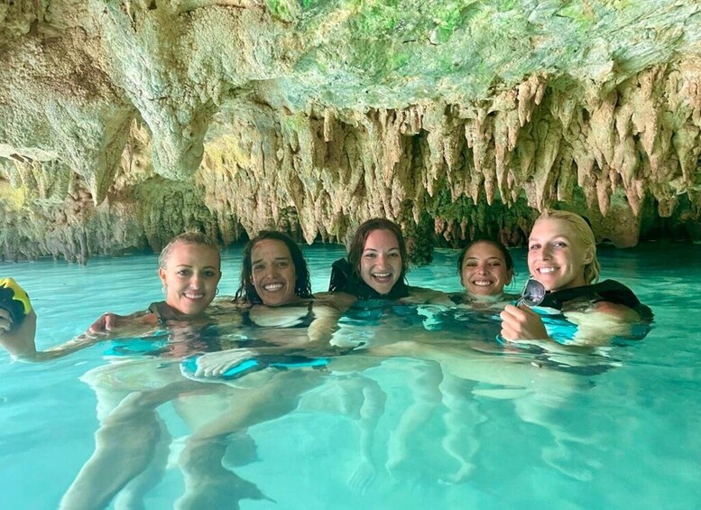 A group of people in a clear blue pool with a cave-like rock formation in the background. 4