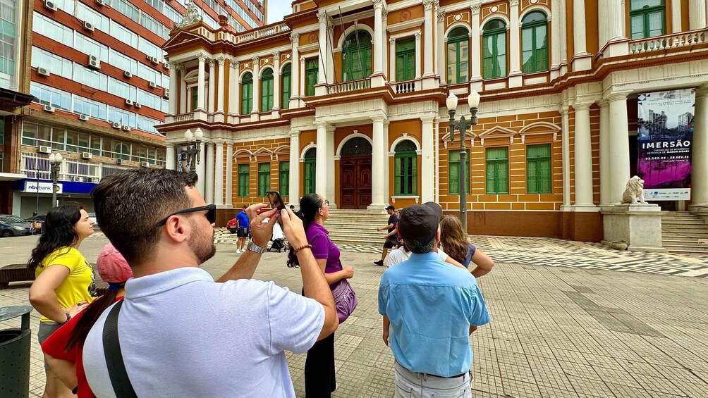 A group of people taking photos in front of a historic building with green windows and a lion statue. 1