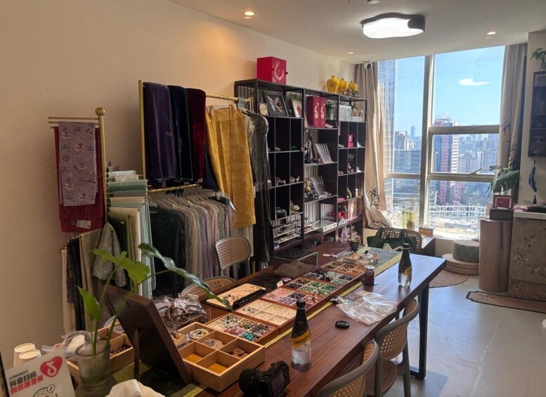 A room with a table displaying various items, a bookshelf filled with books and decorative objects, and a window overlooking a cityscape. 5
