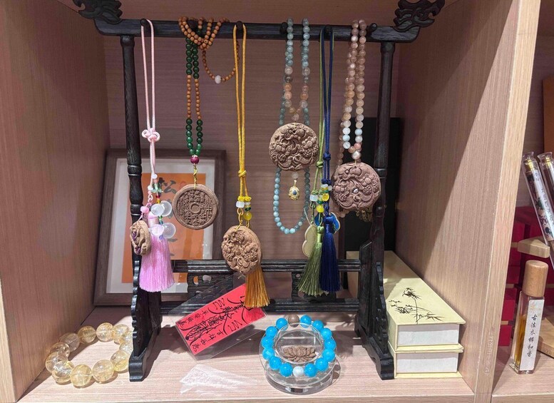 A display of various necklaces and bracelets, including beaded and metallic items, with a red sign and a book in the foreground. 1