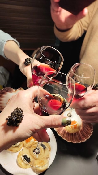 A person holding a wine glass with a red liquid, surrounded by other glasses and a plate with food. 3