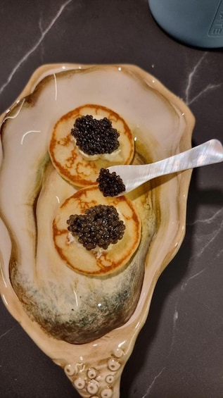 A dish with pancakes topped with caviar in a decorative bowl. 5