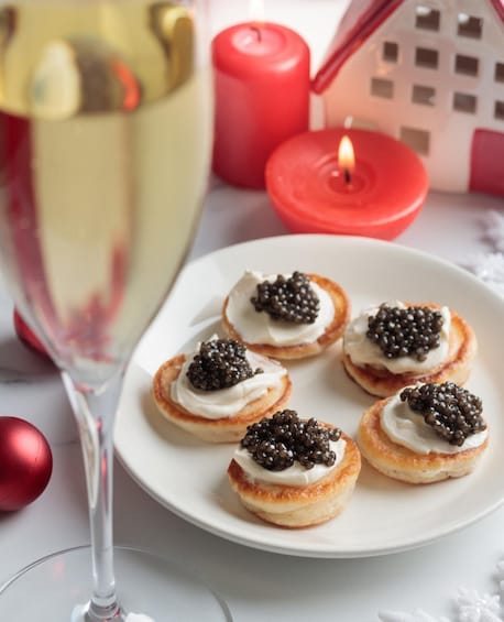A plate of cream puffs with caviar, a glass of champagne, a lit candle, and a red ornament on a table. 2