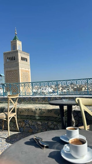 A terrace with a view of a tower, a table with a cup of coffee, and a chair. 4
