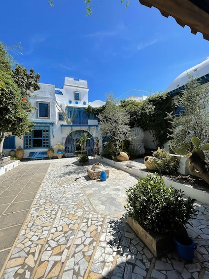 A courtyard with a mosaic floor, white buildings with blue accents, and potted plants. 2