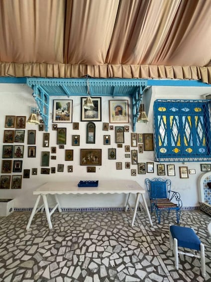 A room with a tiled floor, a white table, blue chairs, and a wall decorated with framed pictures and certificates. 5