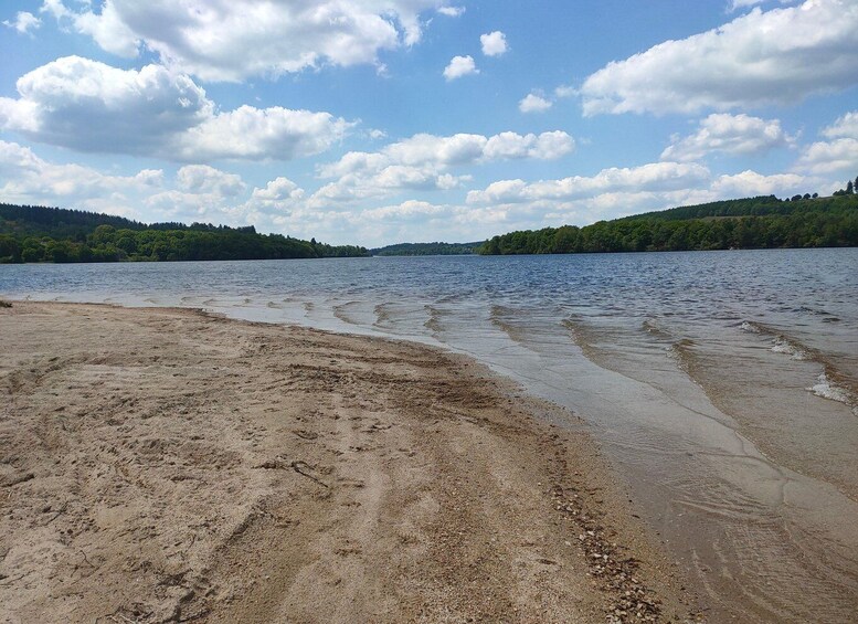 A sandy beach with gentle waves, a clear sky, and forested hills in the background. 4