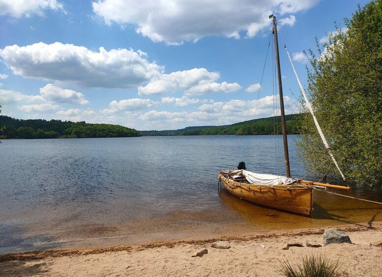 A wooden boat tied to a sandy shore by a calm lake with a forested hill in the background. 1