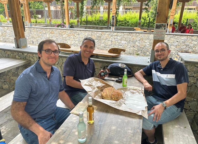 Three men sitting at an outdoor table with food and drinks, surrounded by stone walls and greenery. 5