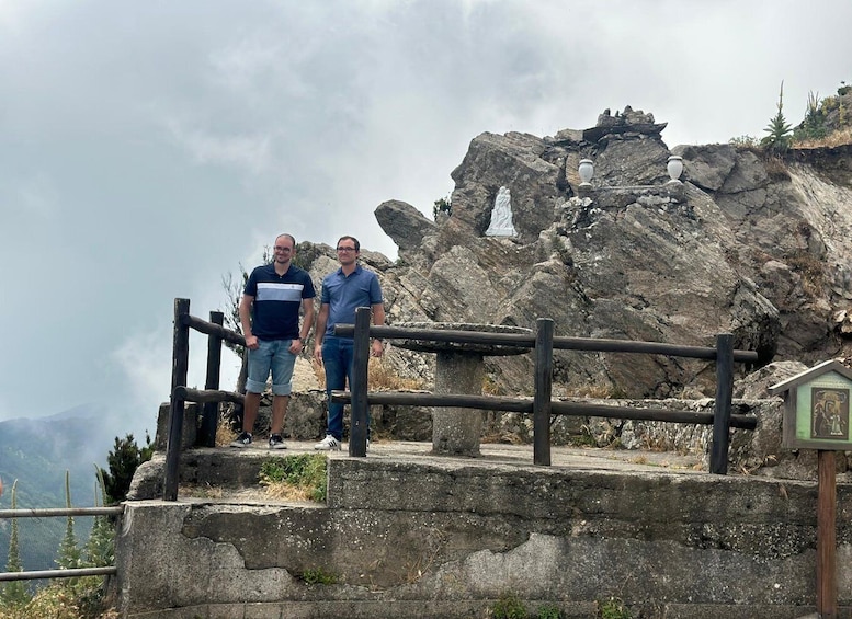 Two people standing on a stone platform with a rocky mountain backdrop. 4
