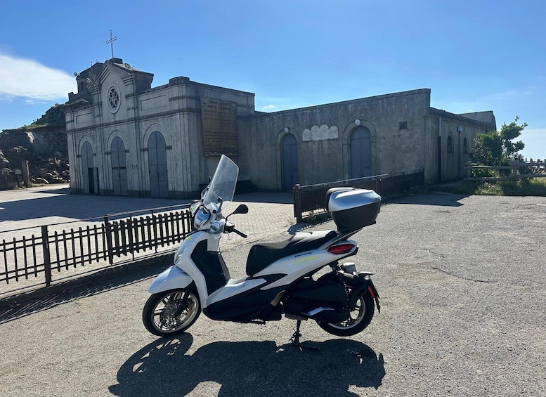 A white scooter parked in front of a church with a cross on top. 1
